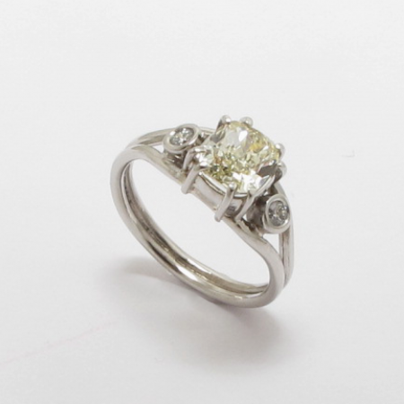 A Handmade Platinum RING set with a Cushion-cut Yellow Diamond (1.20cts.) at centre and 2 Round Brilliant-cut Diamonds (0.06cts.) G/H; VS/SI. Platinum mass 4.6gms.
